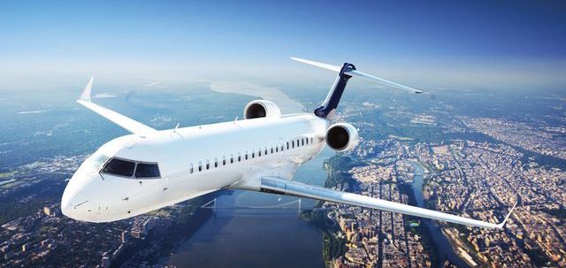 Charter this jet for your next trip A white jet aircraft flying over a cityscape and river.